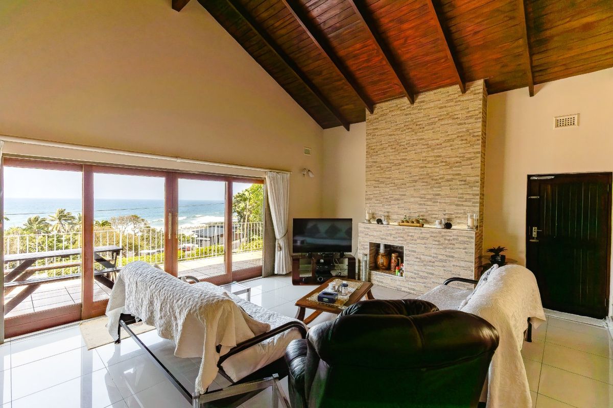 Spacious living room featuring a vaulted timber ceiling, stone-clad fireplace, and large sliding doors opening to a balcony with ocean views.
