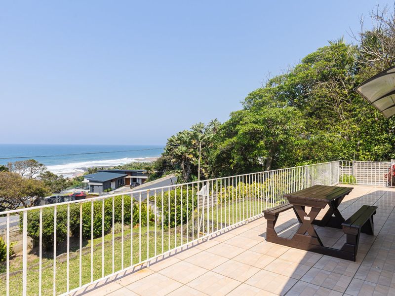 Spacious elevated balcony featuring tiled flooring, a protective metal balustrade, and a polycarbonate awning, offering expansive coastal and ocean views.