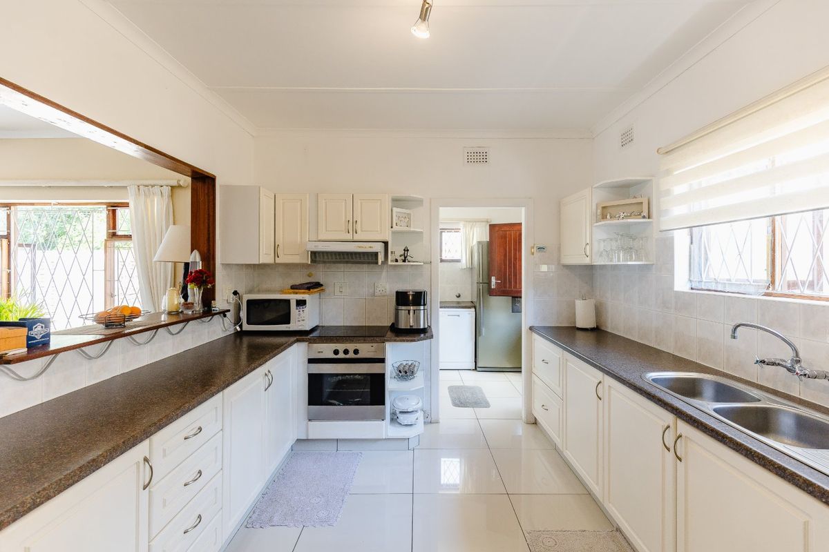 A functional kitchen featuring white cabinetry, dark laminate countertops, a double bowl sink, and a built-in oven with an extractor fan.