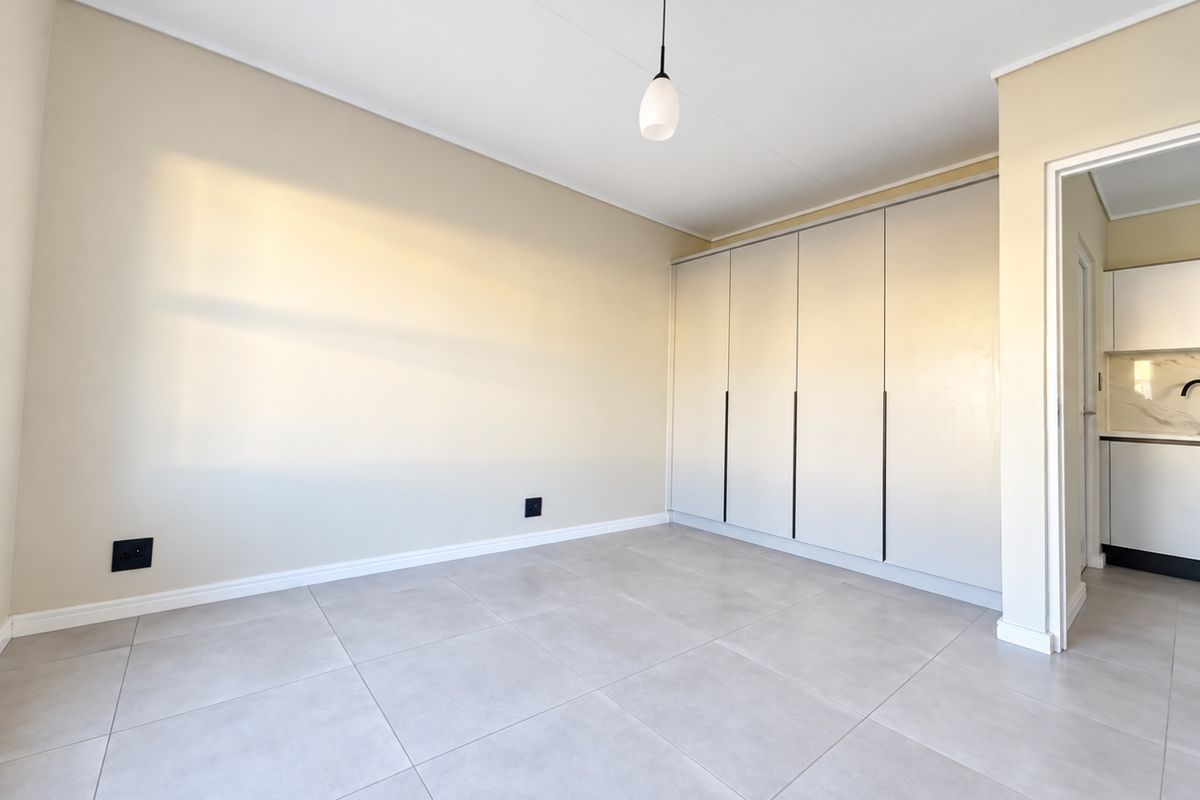 A bright, empty bedroom featuring modern neutral-toned tiled flooring and floor-to-ceiling built-in cupboards, offering a clean and versatile living space.