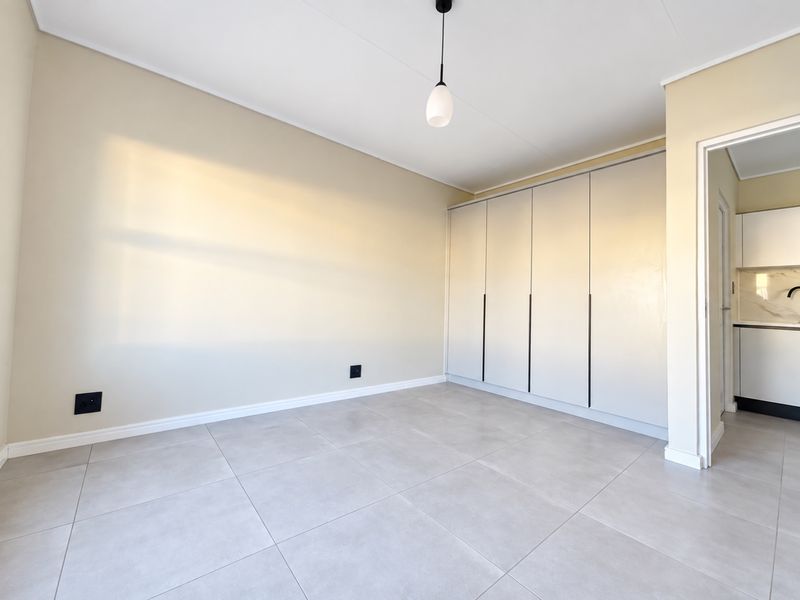 A bright, empty bedroom featuring modern neutral-toned tiled flooring and floor-to-ceiling built-in cupboards, offering a clean and versatile living space.