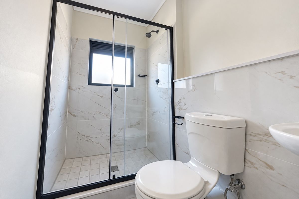 Modern bathroom featuring a walk-in shower with a black-framed glass enclosure, marble-look wall tiling, a white toilet, and a wall-mounted basin.