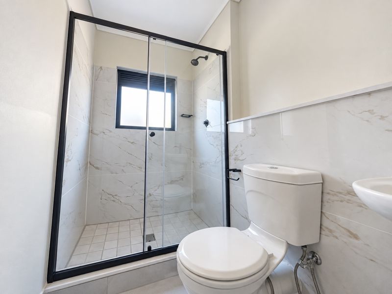 Modern bathroom featuring a walk-in shower with a black-framed glass enclosure, marble-look wall tiling, a white toilet, and a wall-mounted basin.