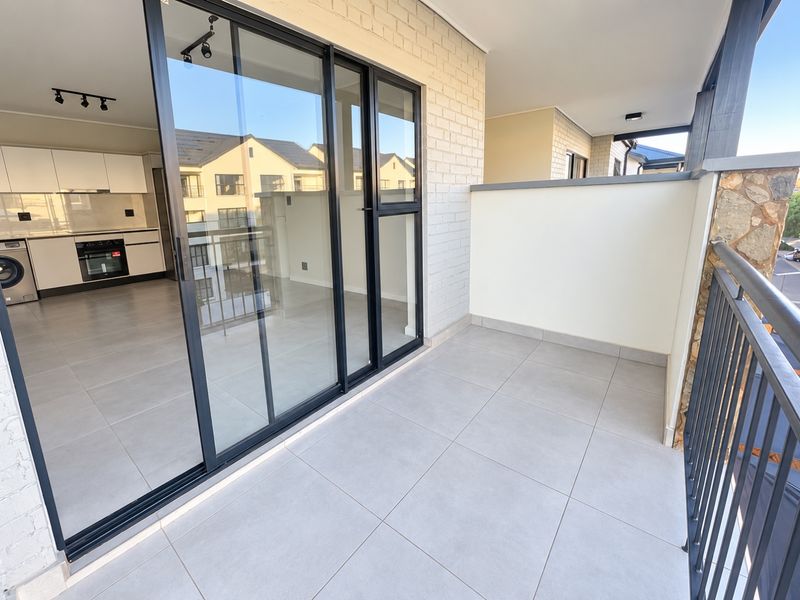 A clean, modern balcony featuring tiled flooring, a metal balustrade, and large sliding glass doors providing access to the interior living space.