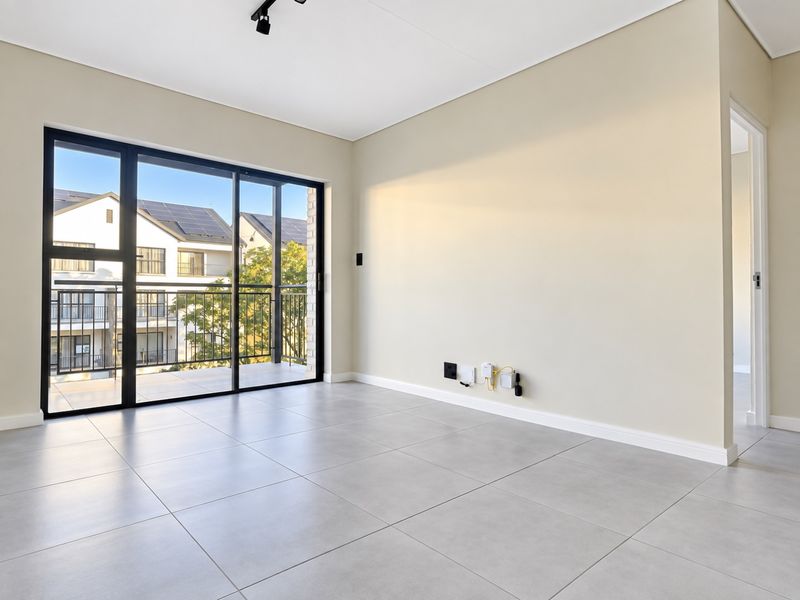 A bright, empty living room featuring large sliding glass doors leading to a balcony, neutral tiled flooring, and modern track lighting.