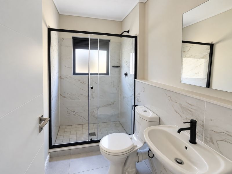 A modern, well-maintained bathroom featuring a walk-in shower with a black frame, marble-look wall tiles, a pedestal basin, and a wall-mounted mirror.