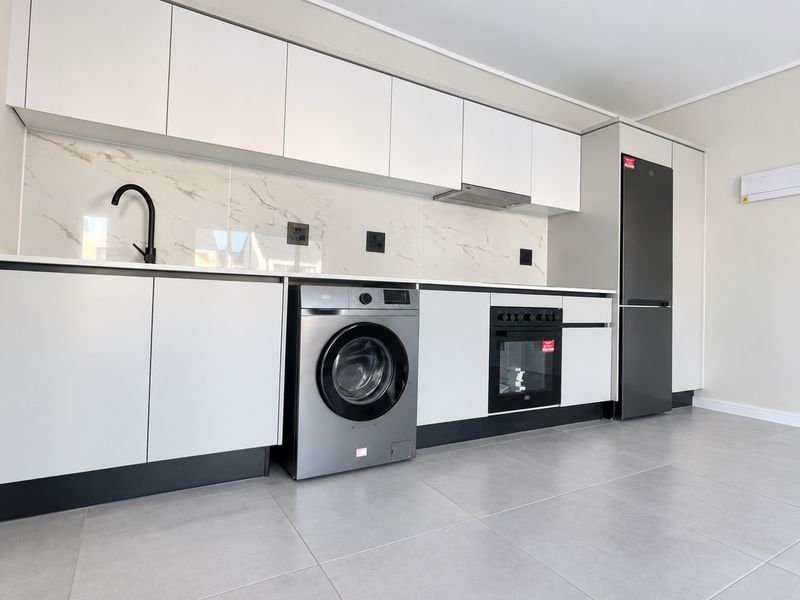 Modern kitchen featuring sleek white cabinetry, marble-look splashback, integrated appliances, and high-quality tiled flooring in a clean, contemporary finish.