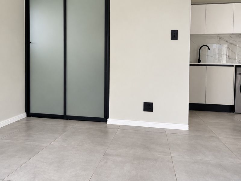 Modern open-plan living area featuring large format grey floor tiles, a sleek sliding glass door, and a glimpse into a contemporary kitchen with marble-look finishes.