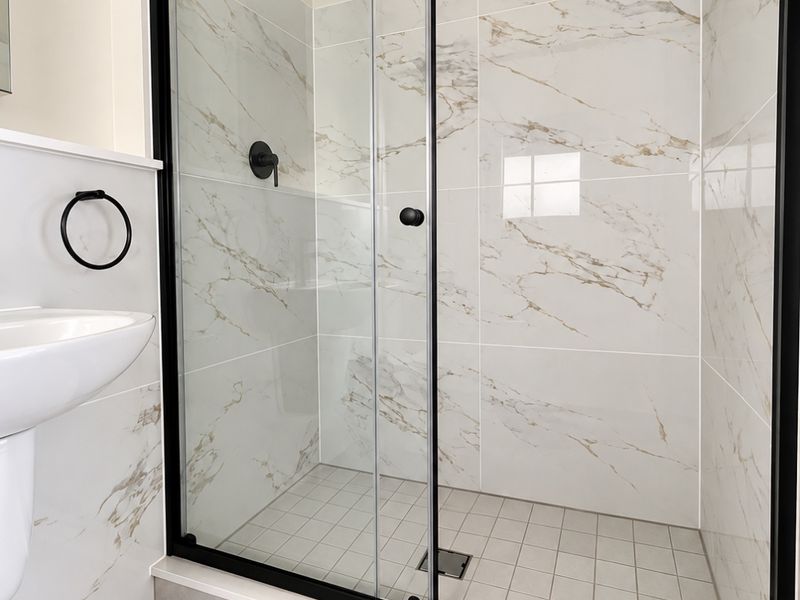 Modern bathroom featuring a walk-in shower with black-framed glass enclosure, marble-look wall tiles, and a pedestal basin.