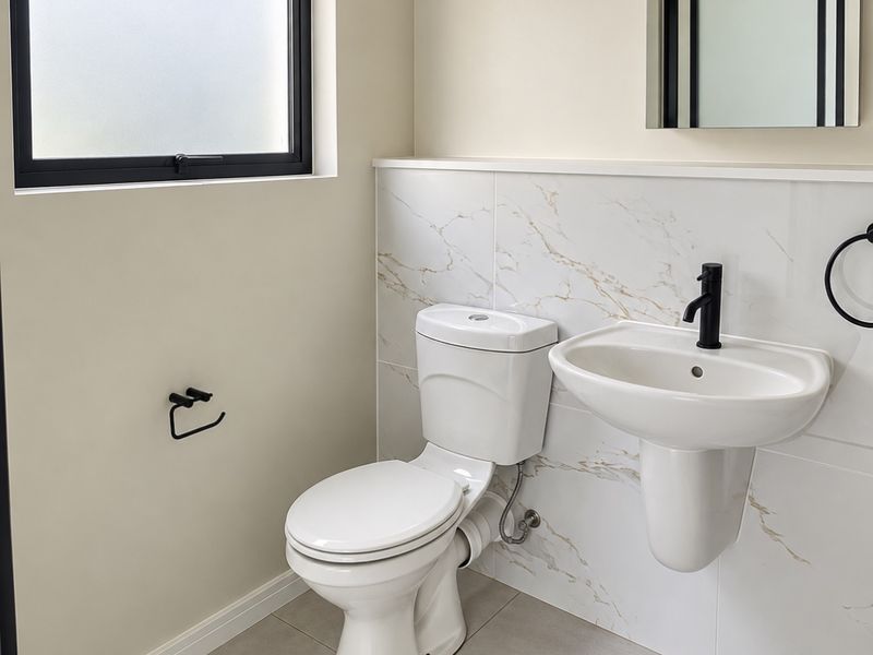 A modern, well-maintained bathroom featuring marble-look wall tiles, a wall-mounted basin with black tapware, and a clean, minimalist aesthetic.
