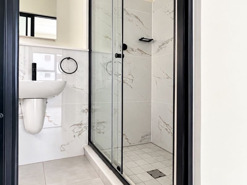 Modern bathroom featuring a walk-in shower with black frame, marble-look wall tiles, and a wall-mounted basin with contemporary black fixtures.