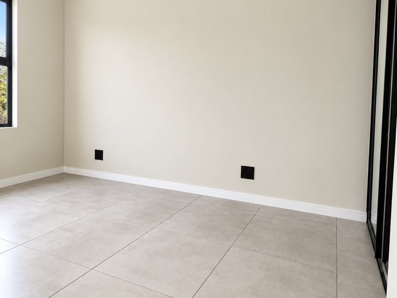 A bright, empty bedroom featuring neutral tiled flooring, clean walls, and a built-in cupboard with a modern black frame.