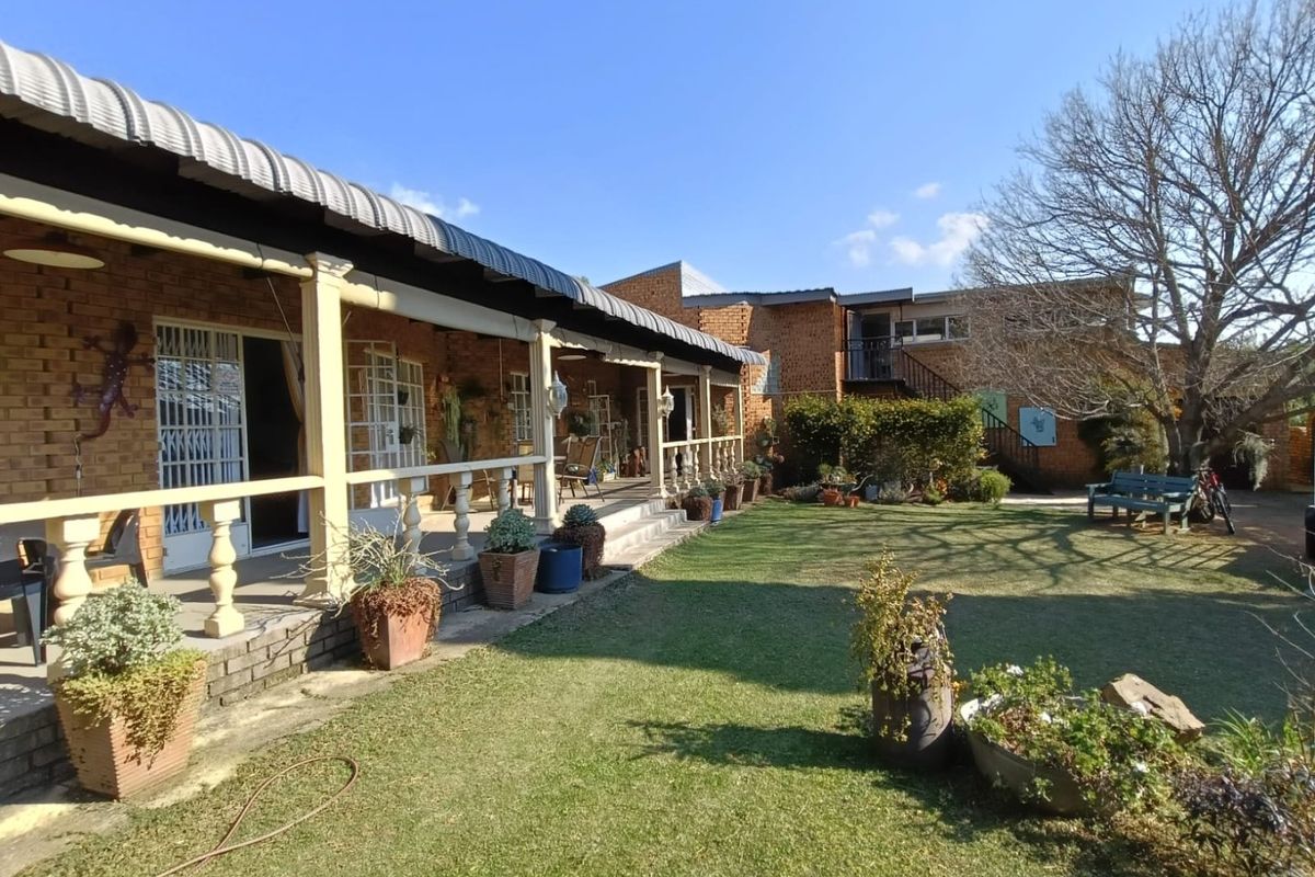 A spacious rear garden featuring a covered patio with a brick facade, balustrades, and an external staircase leading to the upper level.