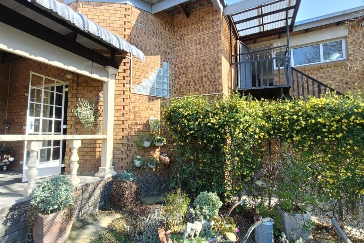 A rear exterior view of a face brick house featuring a covered patio, an external staircase leading to a balcony, and established garden landscaping.