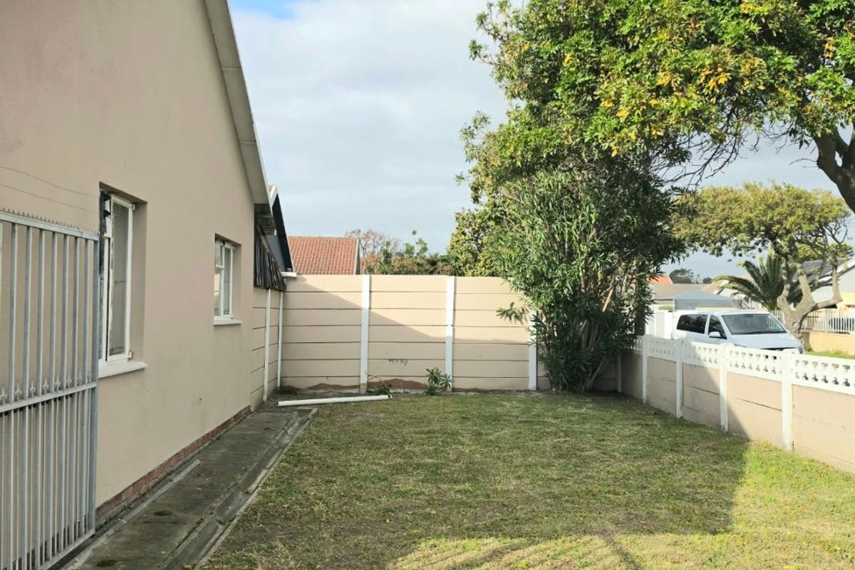 A side garden area featuring a lawn, paved walkway, and precast concrete boundary wall, enclosed by a metal security gate.