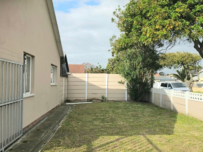 A side garden area featuring a lawn, paved walkway, and precast concrete boundary wall, enclosed by a metal security gate.