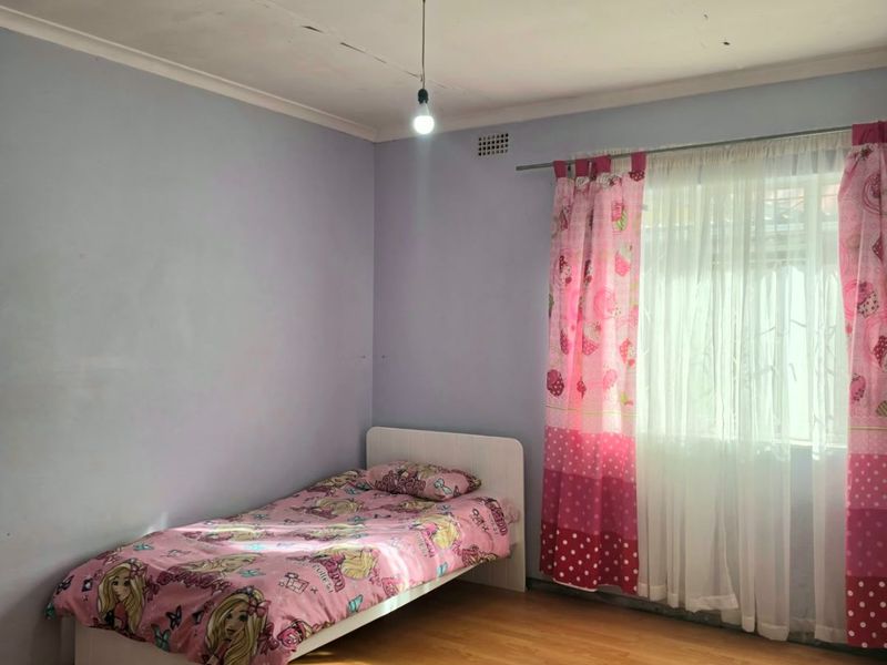 A bedroom featuring laminate flooring and a window with a curtain rod. The ceiling shows visible signs of cracking and paint deterioration.