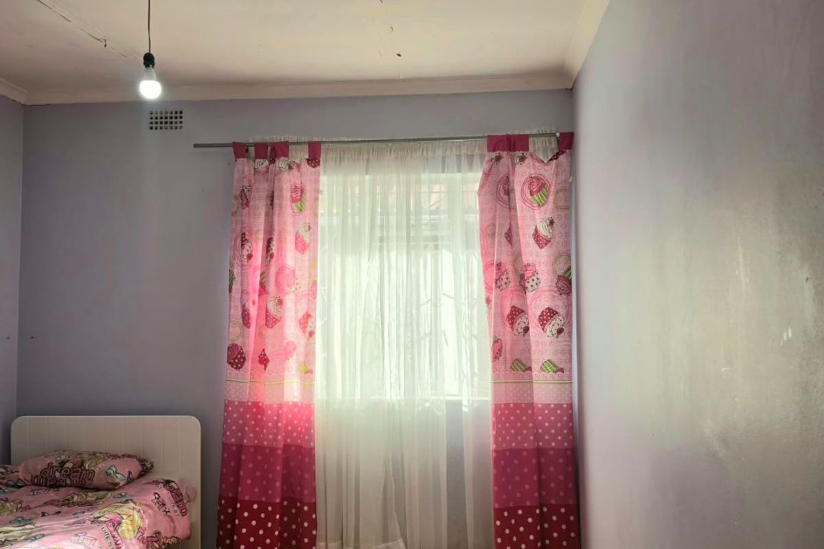 A bedroom featuring laminate flooring and a ceiling ventilation grille, currently requiring cosmetic updates to the walls and ceiling finishes.