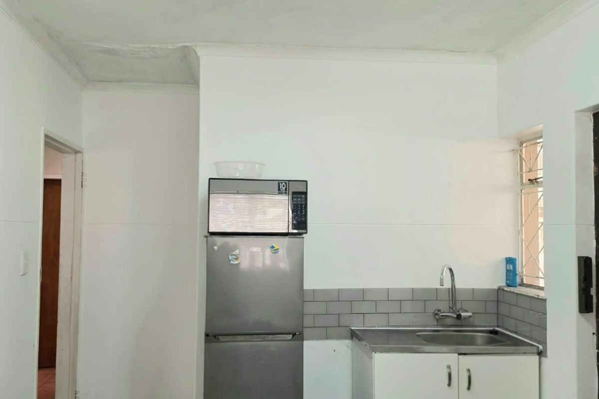 A compact kitchen area featuring a stainless steel sink, tiled backsplash, and ceramic floor tiles, requiring minor ceiling repairs.