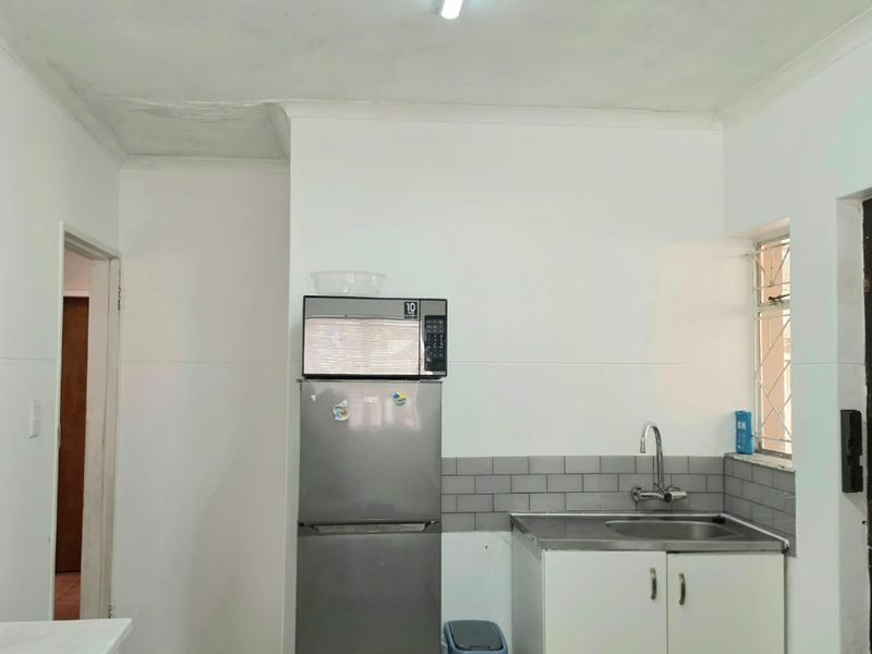 A compact kitchen area featuring a stainless steel sink, tiled backsplash, and ceramic floor tiles, requiring minor ceiling repairs.