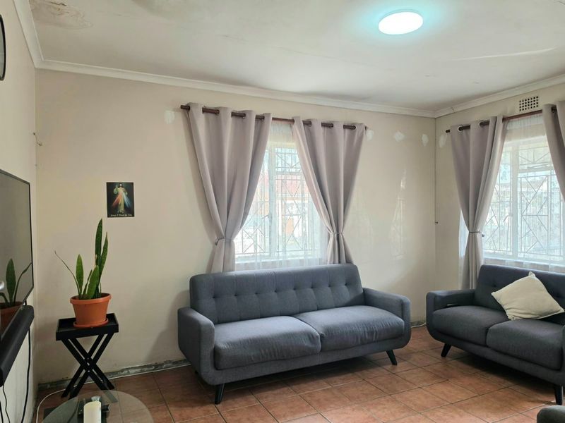 A living room featuring tiled flooring, security bars on windows, and visible ceiling water damage requiring maintenance and cosmetic updates.