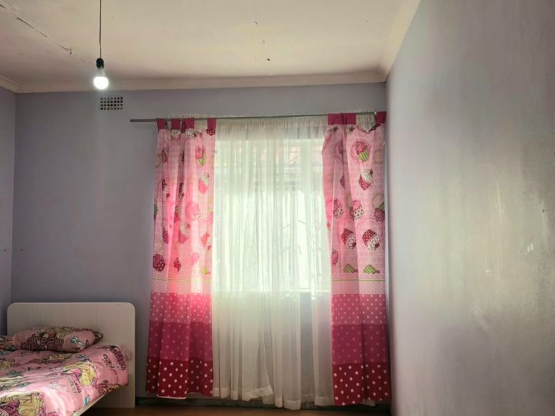 A bedroom featuring laminate flooring and a ceiling ventilation grille, currently requiring cosmetic updates to the walls and ceiling finishes.