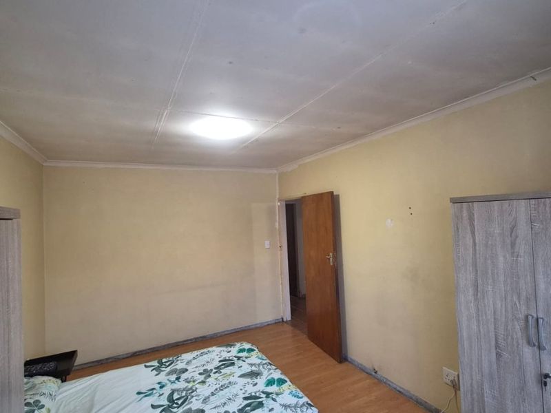 A bedroom featuring laminate flooring and a simple ceiling light fixture, requiring cosmetic updates to the walls and ceiling to improve the overall aesthetic.