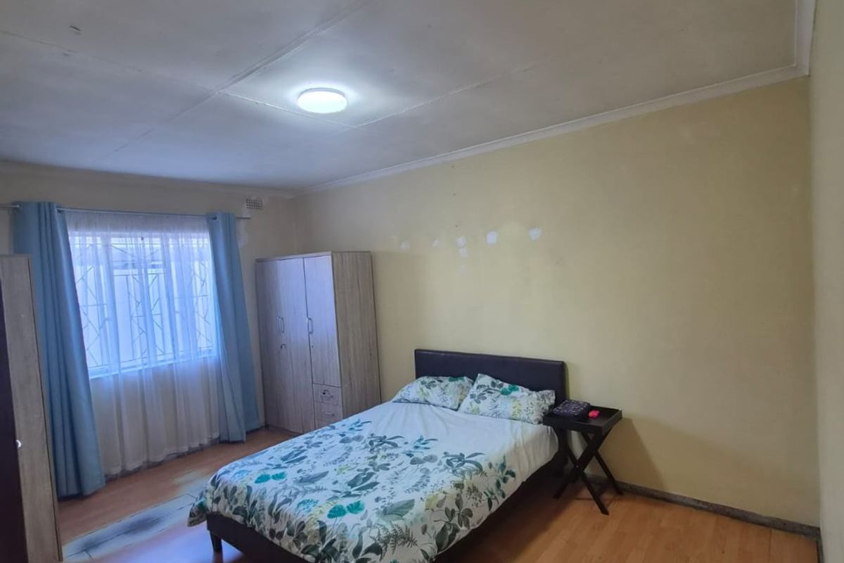 A bedroom featuring laminate flooring and security bars on the window, requiring minor wall repairs and cosmetic updates to improve the overall finish.