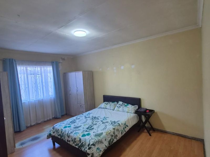 A bedroom featuring laminate flooring and security bars on the window, requiring minor wall repairs and cosmetic updates to improve the overall finish.