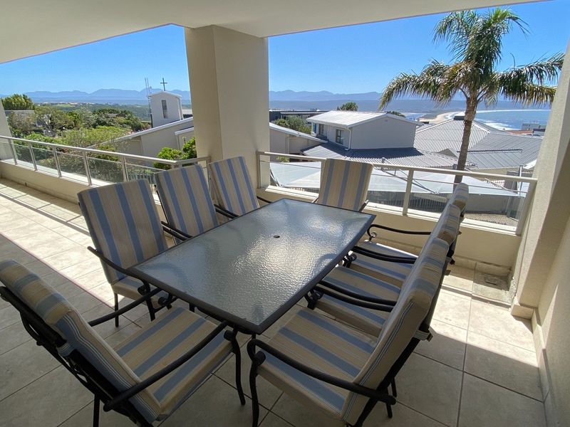 Spacious covered balcony featuring tiled flooring and a glass balustrade, offering scenic coastal and mountain views.