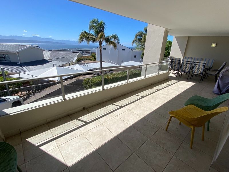 Spacious covered balcony featuring tiled flooring and a modern glass balustrade, offering scenic coastal and mountain views.