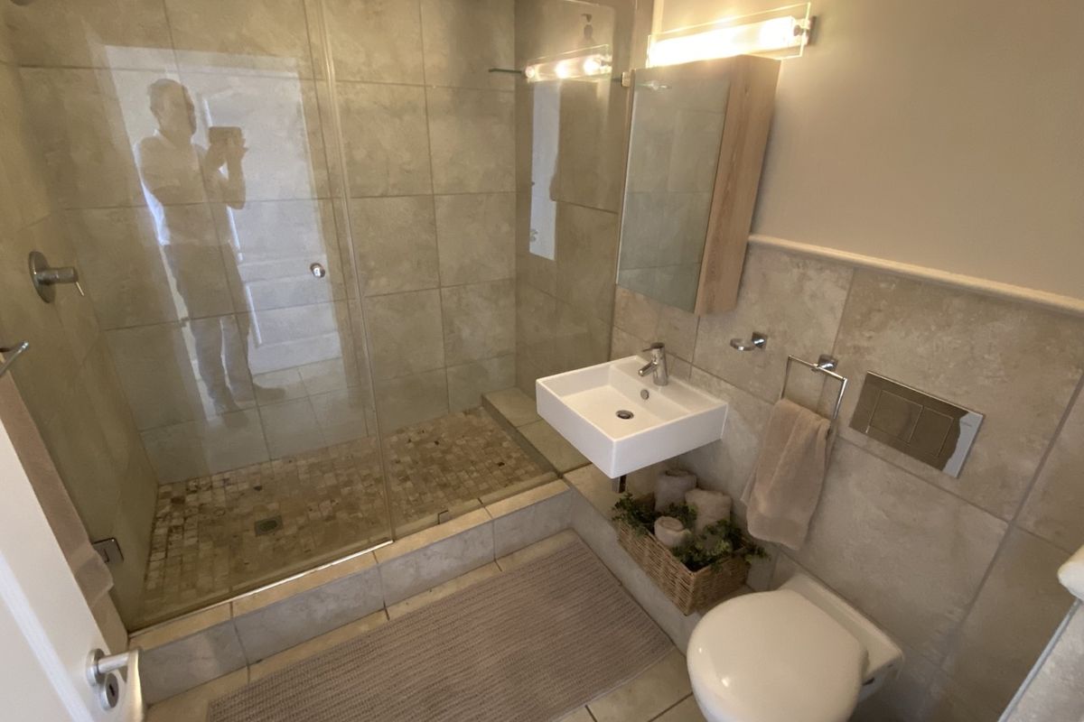 Modern bathroom featuring a glass-enclosed shower with tiled flooring, a wall-mounted basin, and a wall-mounted toilet with integrated flush plate.