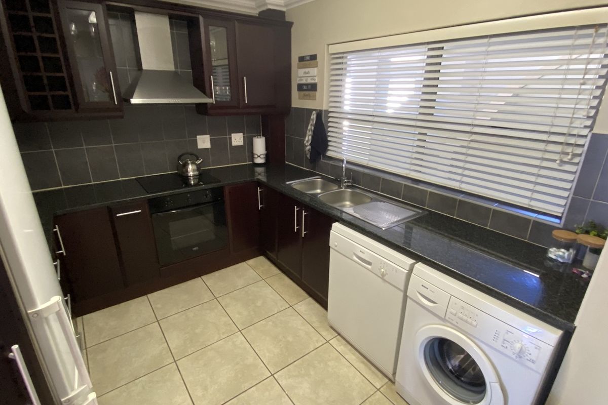 A functional kitchen featuring dark wood cabinetry, granite countertops, a built-in oven with hob, and a double basin sink with tiled finishes.