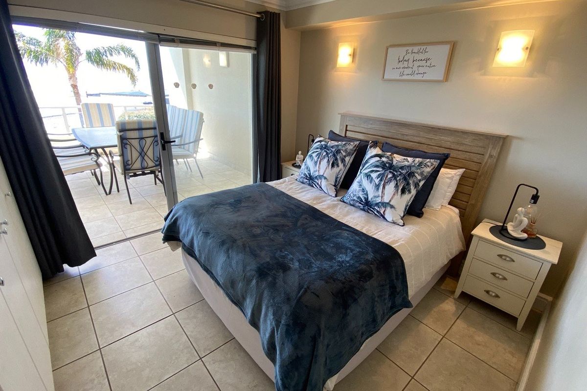 A well-maintained bedroom featuring tiled flooring, wall-mounted lighting, and a large sliding glass door providing direct access to a private balcony.