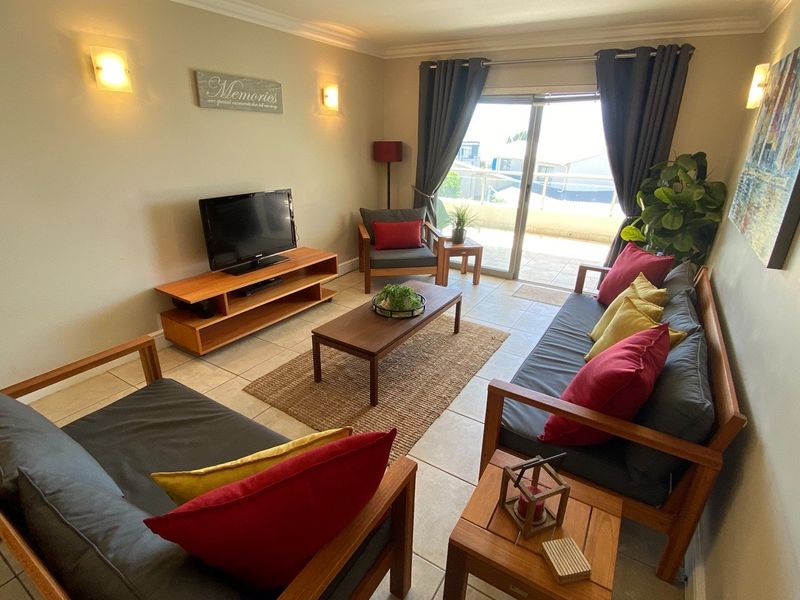 A comfortable living room featuring tiled flooring, wall-mounted lighting, and a sliding glass door providing access to an outdoor balcony area.