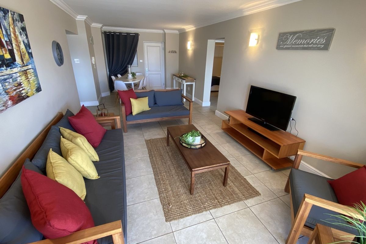 A well-maintained living room featuring neutral tiled flooring, crown molding, and wall-mounted lighting, creating a comfortable and inviting atmosphere.