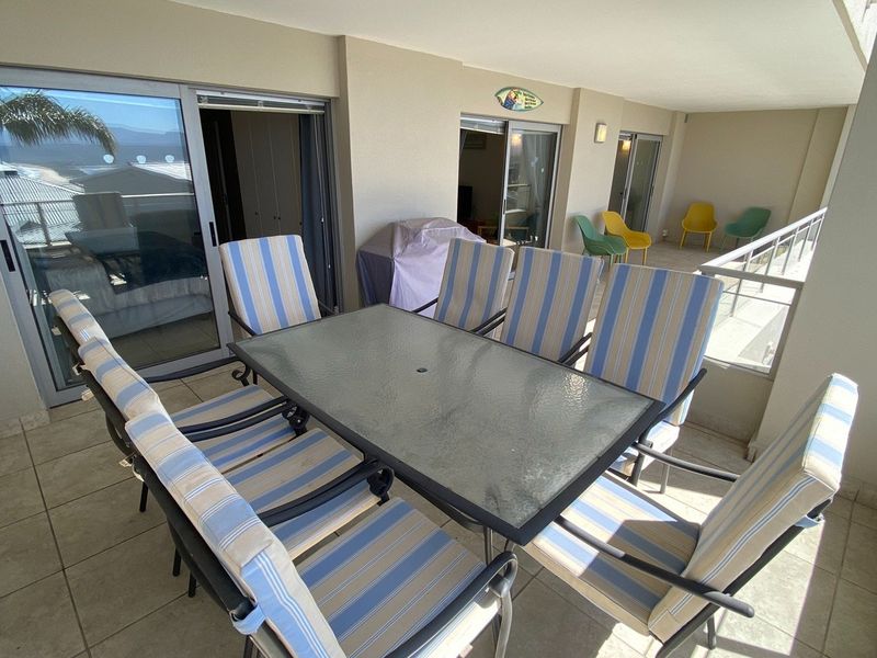 A spacious covered balcony featuring tiled flooring, metal railings, and multiple sliding glass door access points to the interior living areas.