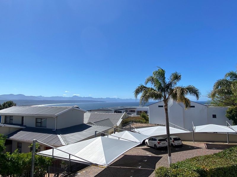 Elevated view overlooking a residential complex with shade-covered parking and a scenic coastal mountain backdrop.