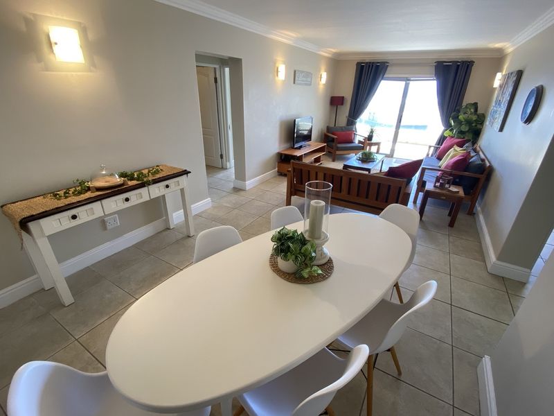 Open-plan living and dining area featuring neutral tiled flooring, wall-mounted lighting, and a sliding glass door providing access to the exterior.