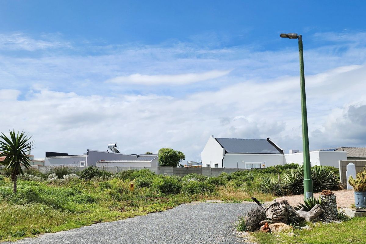 A vacant residential plot featuring a gravel driveway, established boundary wall, and street lighting, situated in a developed neighborhood.