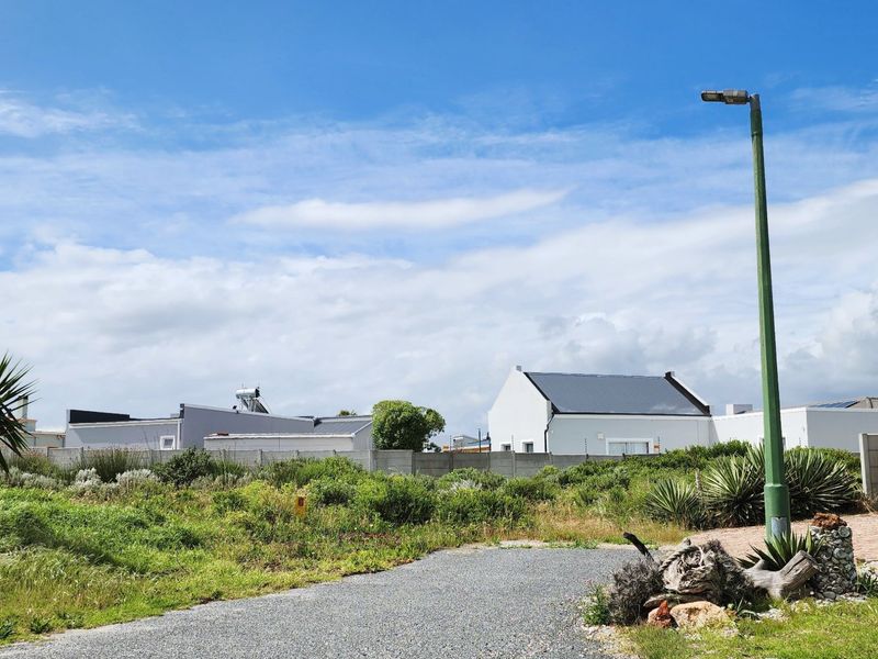 A vacant residential plot featuring a gravel driveway, established boundary wall, and street lighting, situated in a developed neighborhood.