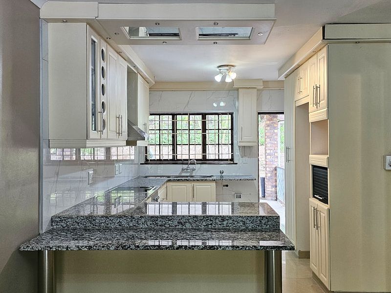 A well-maintained kitchen featuring granite countertops, ample built-in cabinetry, a tiled backsplash, and integrated appliances, offering a clean and functional workspace.