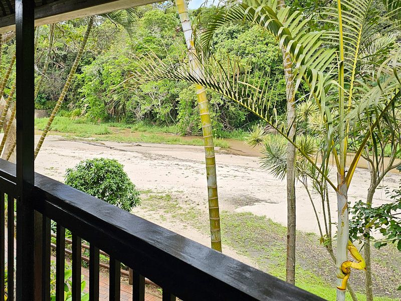 A covered balcony featuring a timber railing, offering a peaceful view of the surrounding natural landscape and riverbed.
