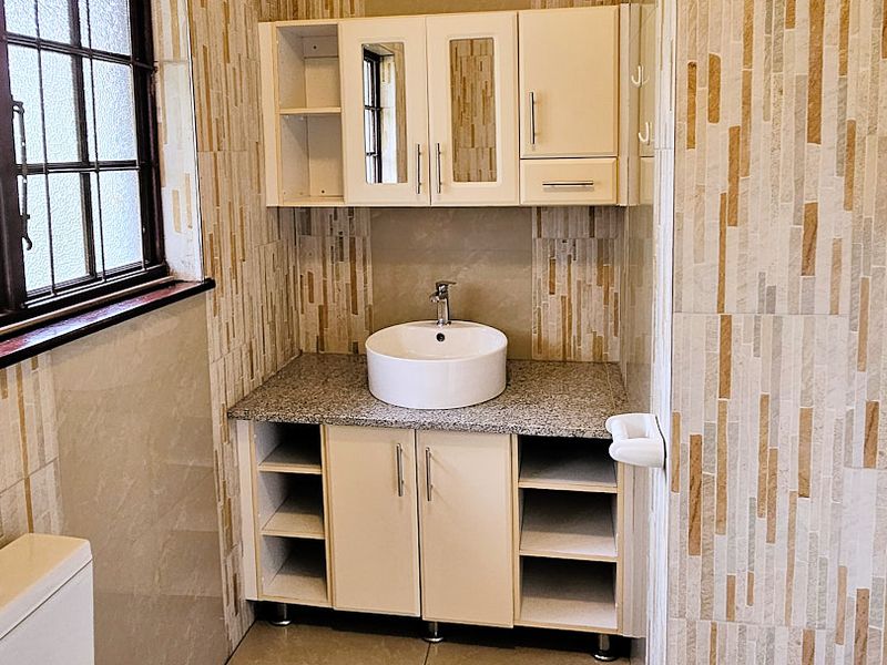A clean bathroom featuring a vessel sink on a granite vanity, wall-mounted storage cabinets, and decorative tiled wall finishes.