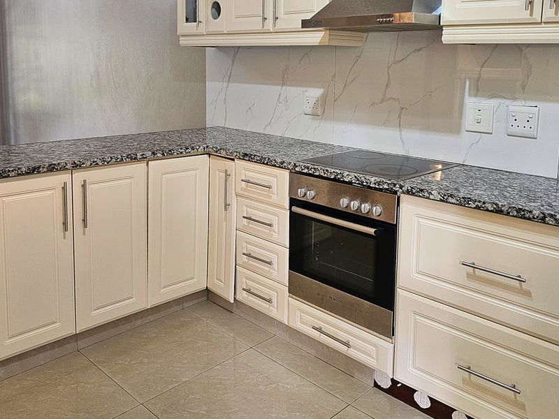 A clean, modern kitchen featuring granite countertops, shaker-style cabinetry, a built-in oven with electric hob, and a stylish marble-look splashback.