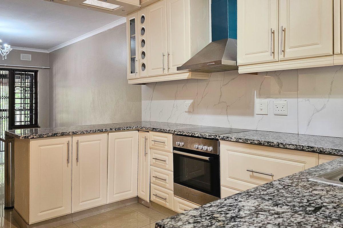 Modern kitchen featuring granite countertops, built-in oven, electric hob, stainless steel extractor fan, and ample cabinetry with a marble-look splashback.