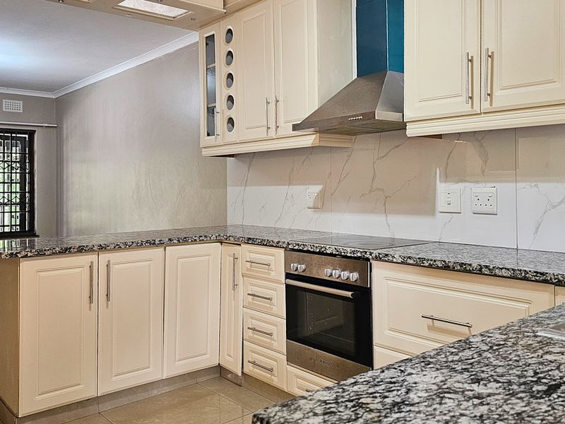 Modern kitchen featuring granite countertops, built-in oven, electric hob, stainless steel extractor fan, and ample cabinetry with a marble-look splashback.