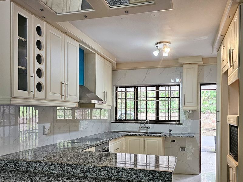 A well-maintained kitchen featuring granite countertops, ample built-in cabinetry, a tiled backsplash, and a functional layout with direct access to the exterior.