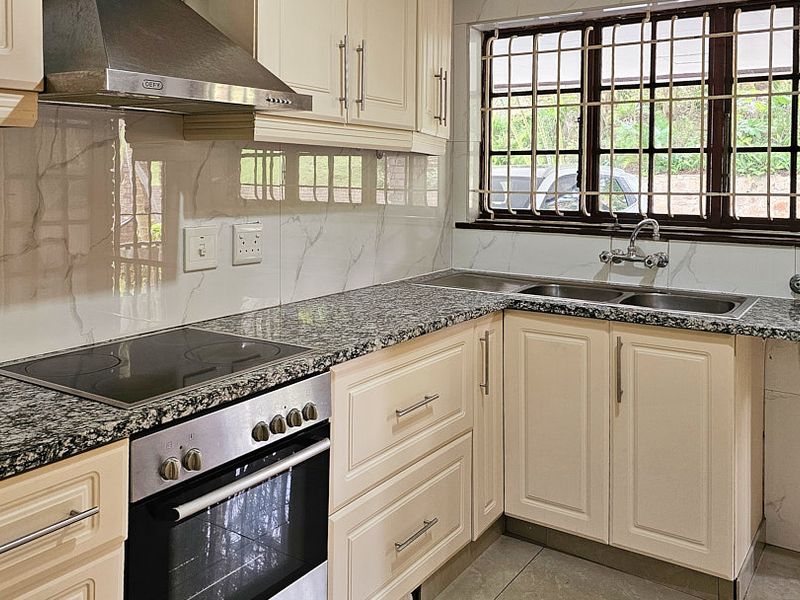 A well-maintained kitchen featuring granite countertops, built-in oven, electric hob, stainless steel extractor fan, and double basin sink with tiled splashback.