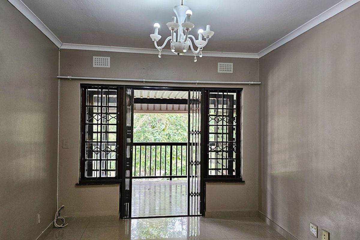 An empty living room featuring tiled flooring, security gates leading to a balcony, and neutral wall finishes, offering a blank canvas for personalization.